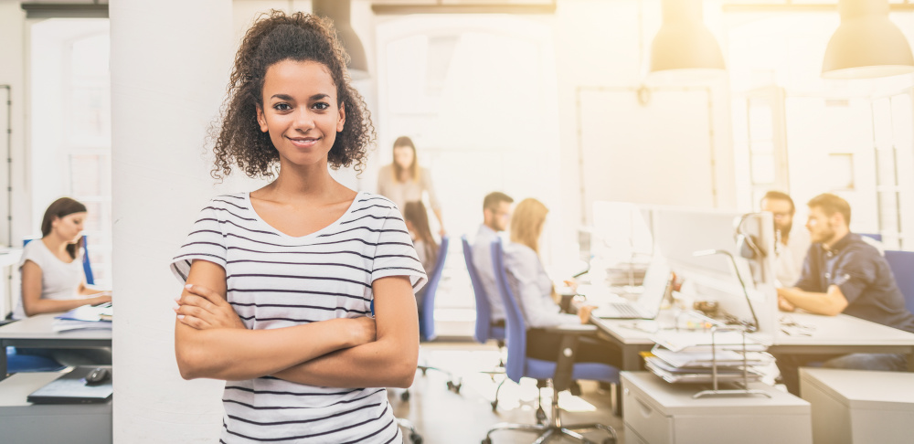 Young professional woman smiling for the camera with office coworkers in the background